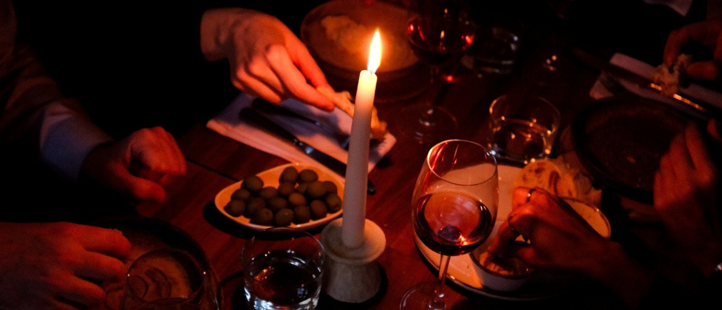 Two glasses of red wine beside a candle on a wooden table