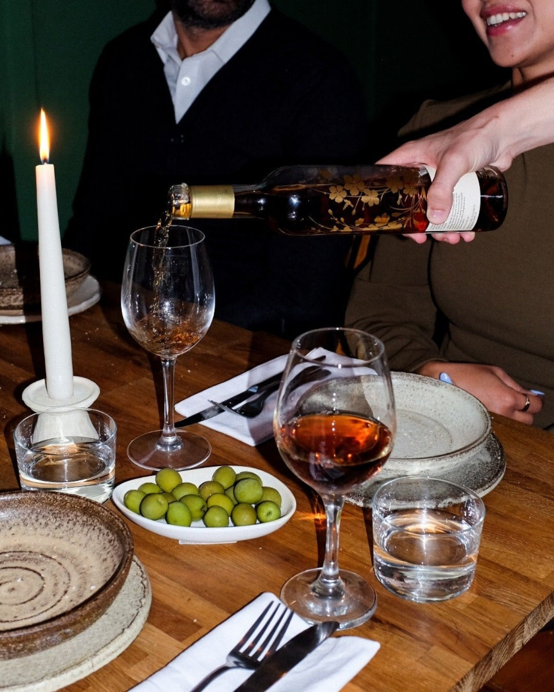 Wine poured at a candlelit table set with olives